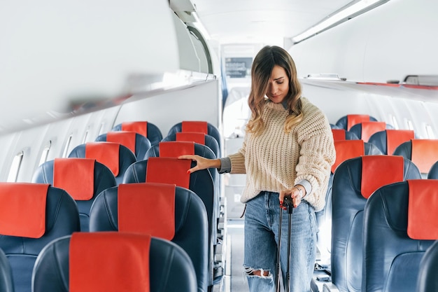 Tenendo il bagaglio il giovane passeggero femminile in abiti casual è nell'aereo