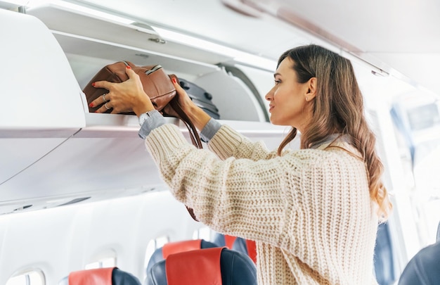 Photo holding lugagge young female passanger in casual clothes is in the plane