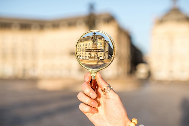 Tenendo una lente di ingrandimento focalizzata sulla famosa fontana delle tre grazie in piazza la bourse durante la mattinata nella città di bordeaux, francia
