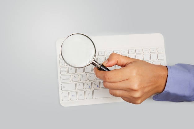 Holding a magnifying glass on a keyboard. Business and cyber security concept. High angle view.