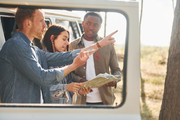 Holding map and looking for location Group of young people is traveling together in the forest