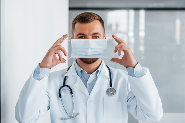 Фото Держащая маска профессиональный медик в белом халате находится в клинике