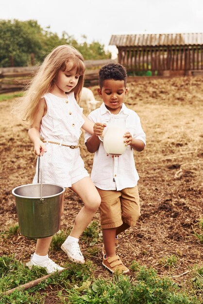 Холдинг молоко Милый маленький африканский американец с европейской девочкой на ферме