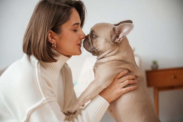 ペットを手に愛と世話をしている若い女性はパグ犬と一緒に家にいます