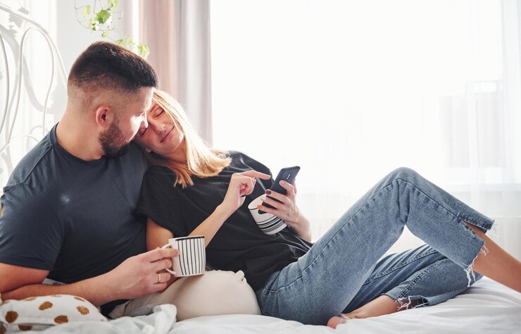 Photo holding phone and cup of drink. young married couple have leisure together in bedroom at daytime.