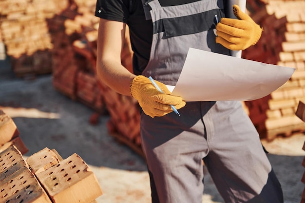 Holding plan in hands Construction worker in uniform and safety equipment have job on building