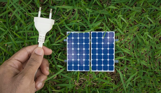 Holding a plug wire next to a photovoltaic solar panel on grass background Alternative clean energy concept