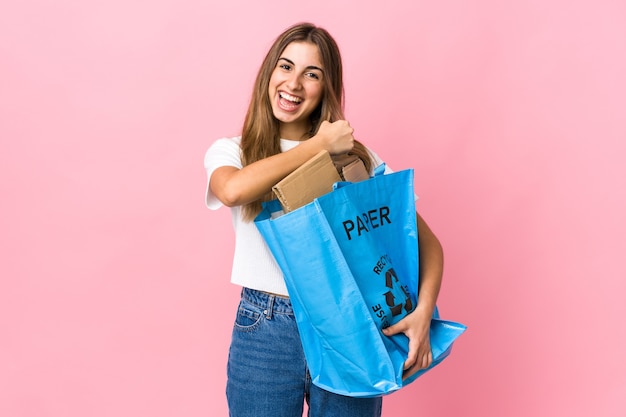 Holding a recycling bag full of paper to recycle over isolated pink celebrating a victory