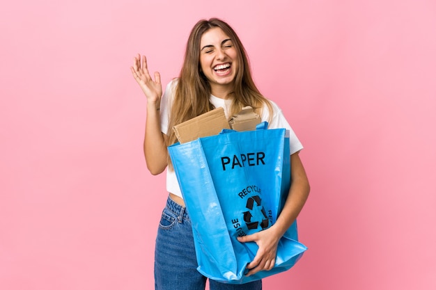 Holding a recycling bag full of paper to recycle over isolated pink laughing