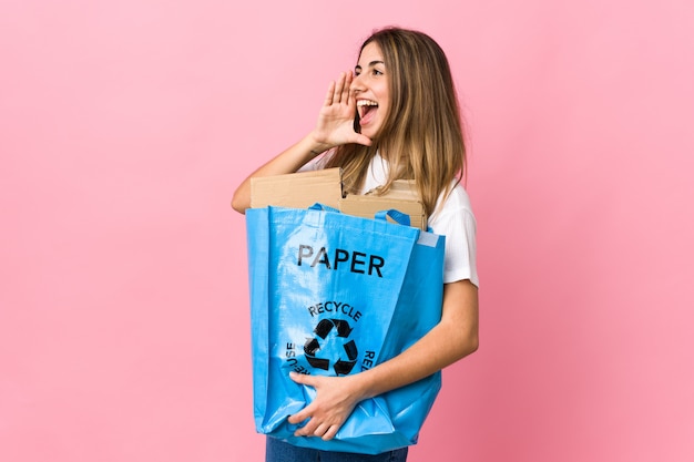 Holding a recycling bag full of paper to recycle over isolated pink shouting with mouth wide open