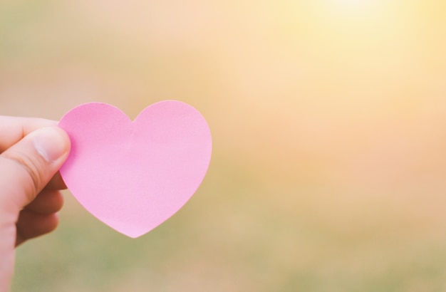 Holding a red heart in hands on green background.