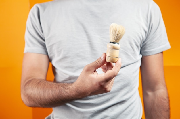 Holding a shaving brush in his hand on an orange background