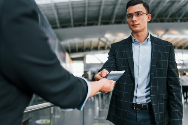 Holding and showing vaccination certificate young businessman\
in formal clothes is in the airport at daytime