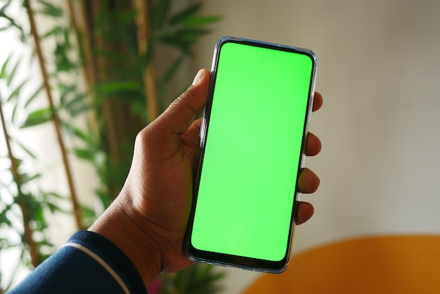 holding smart phone with green screen and home interior decoration on table