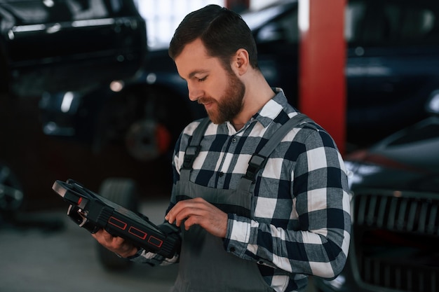 Holding tablet Man in uniform is working in the auto salon