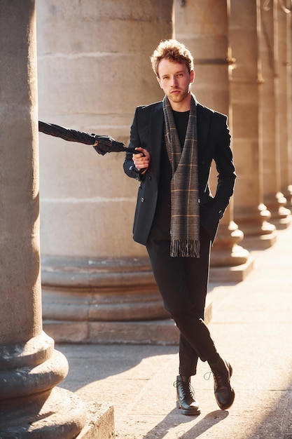 Holding umbrella Elegant young man in formal classy clothes outdoors in the city