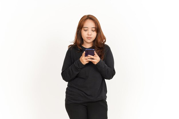 Tenendo e utilizzando lo smartphone di una bella donna asiatica che indossa una camicia nera isolata su bianco
