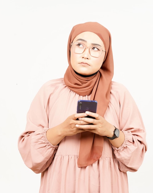 白い背景で隔離のヒジャーブを身に着けている美しいアジアの女性のスマート フォンを保持または使用