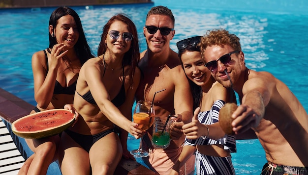 Holding watermelon Group of young happy people have fun in swimming pool at daytime