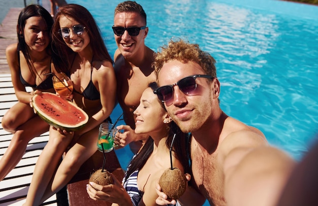 Photo holding watermelon group of young happy people have fun in swimming pool at daytime