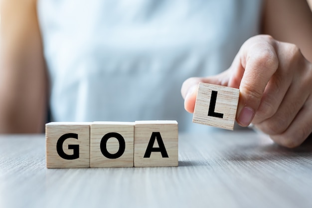 holding wooden cube with GOAL text on table background. 