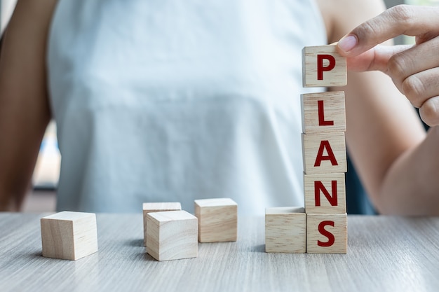 holding wooden cube with PLAN text on table 