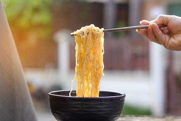 Photo holding yellow noodles hand-held wooden chopsticks on a bowl