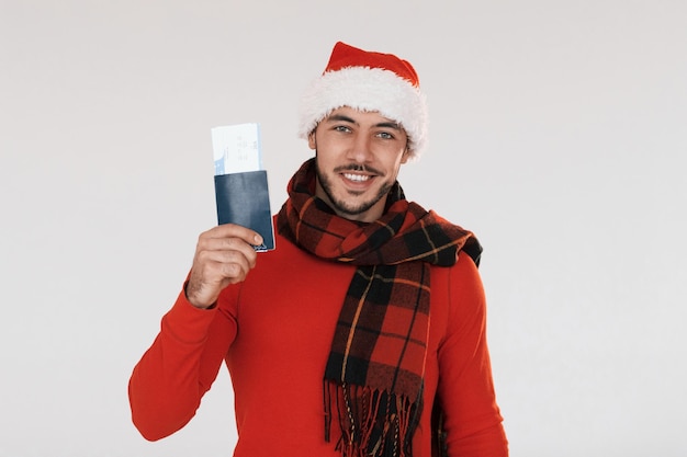 Holds airplane ticket Young handsome man in New year clothes standing indoors against white background