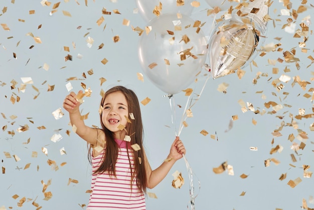 Holds balloons Happy little girl standing and have fun indoors at birthday party