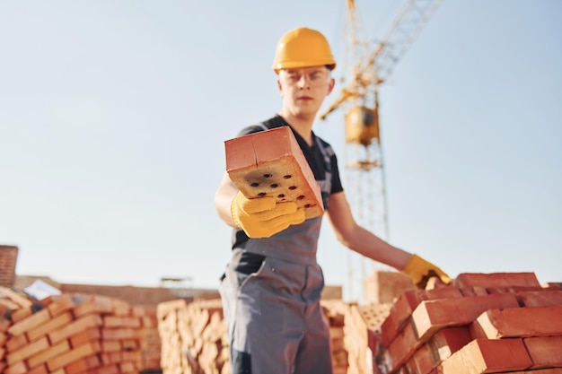 Holds brick in hand Construction worker in uniform and safety equipment have job on building