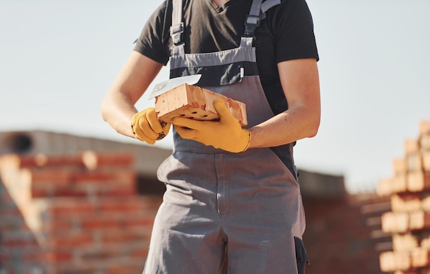 Holds brick in hands Construction worker in uniform and safety equipment have job on building