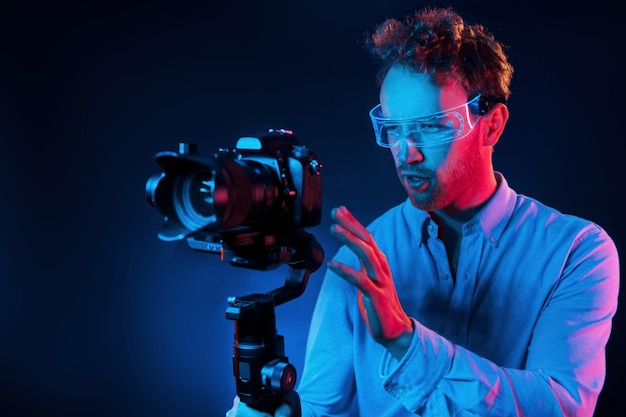 Holds camera Neon lighting Young european man is in the dark studio