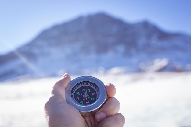 Holds a compass against the backdrop of a mountain