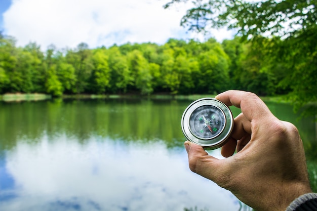 Holds a compass of a lake and forest during the day