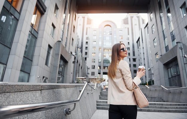 Holds cup of drink Beautiful young european woman is outdoors in the city at daytime