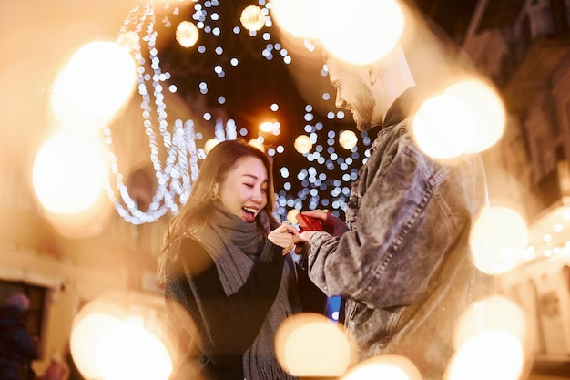 Holds gift box Happy multiracial couple together outdoors in the city celebrating New year