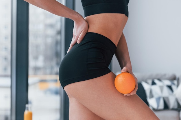 Holds healthy food in hands Young woman with slim body shape in black sportswear have fitness day indoors at home