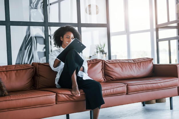 Holds notepad Young african american woman with curly hair indoors at home