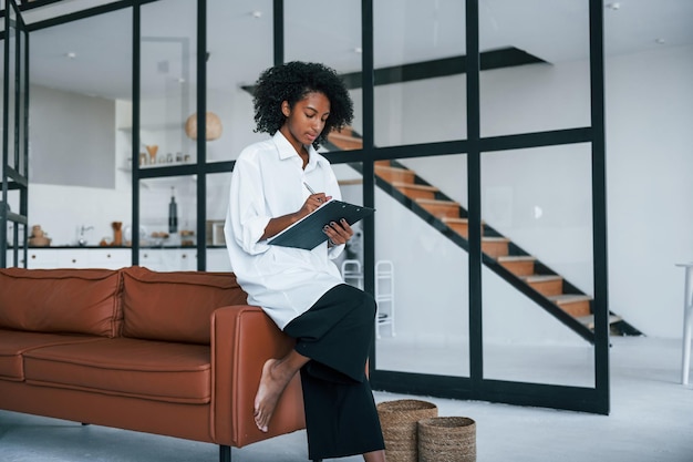 Holds notepad Young african american woman with curly hair indoors at home