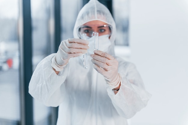 Holds test tubes. portrait of female doctor scientist in lab coat, defensive eyewear and mask