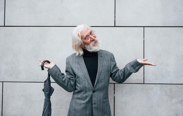 Holds umbrella Senior businessman in formal clothes with grey hair and beard is outdoors