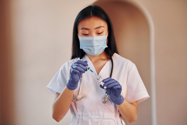 Holds vaccine and syringe Young serious asian woman standing indoors