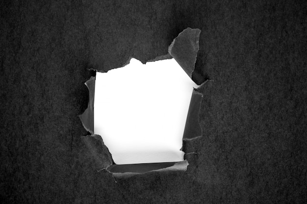 Hole in the black paper with torn sides 