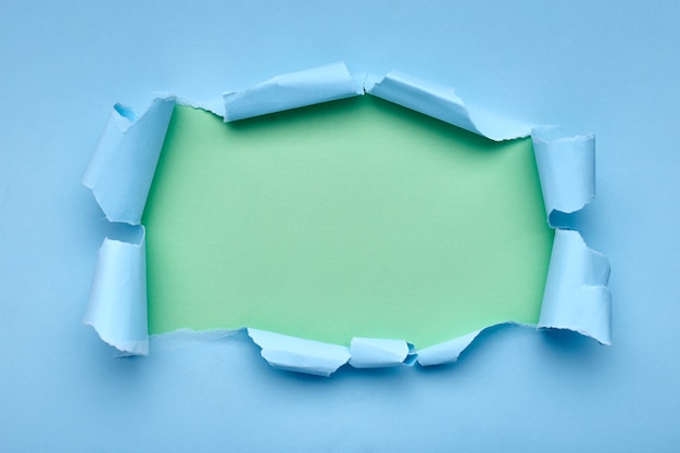 Hole in the blue paper. Torn. Green . Abstract .