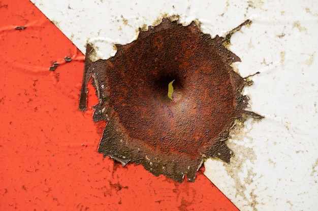 The hole in the metal is covered with rust. Damaged road sign.