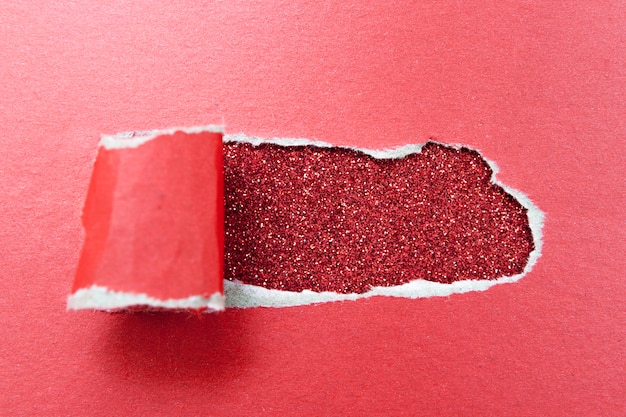 Hole in a sheet of red paper on a glittery surface