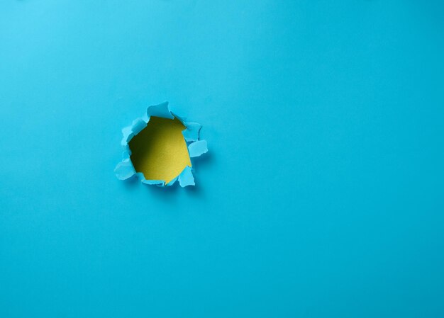 Hole with torn edges in blue paper, full frame. Copy space