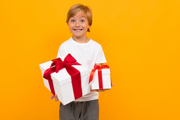 Фото Праздничный день . привлекательный мальчик протягивает коробочку с подарком с красной лентой на ярко-желтом