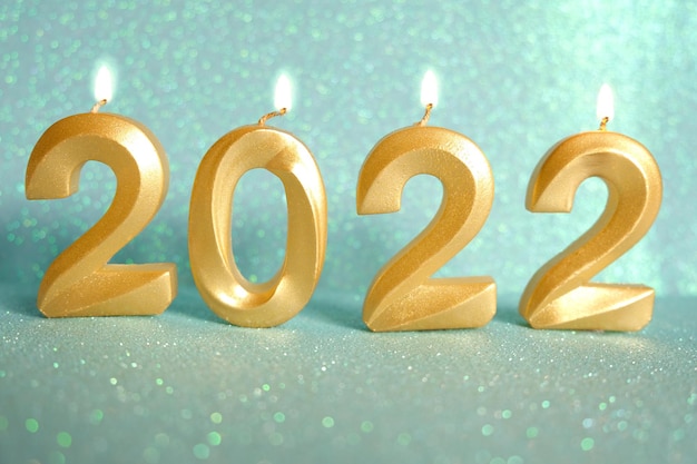 Holiday background Happy New Year 2022. Numbers of year 2022 made by gold candles on bokeh festive sparkling background. celebrating New Year holiday, close-up. Burning numbers