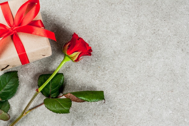 Holiday  background, Valentine's day. Bouquet of red roses, tie with a red ribbon, with wrapped gift box and red candle. On a gray stone table, copy space top view